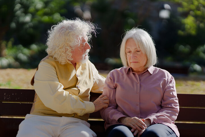 man comforting a woman with dementia on a bench