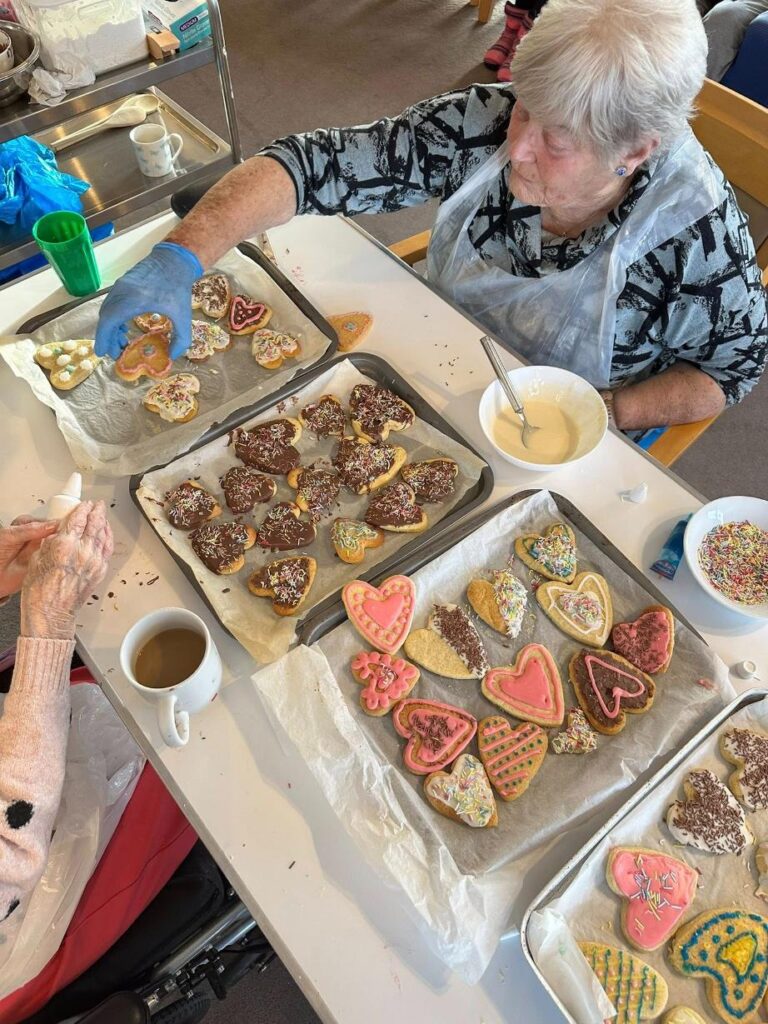 Elderly woman decorating heart-shaped biscuits with chocolate, pink icing and sprinkles