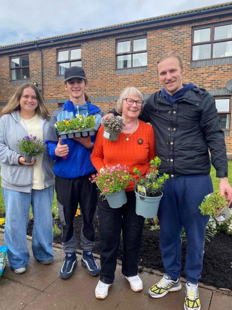 family of four smiling while holding pots of flowers to plant
