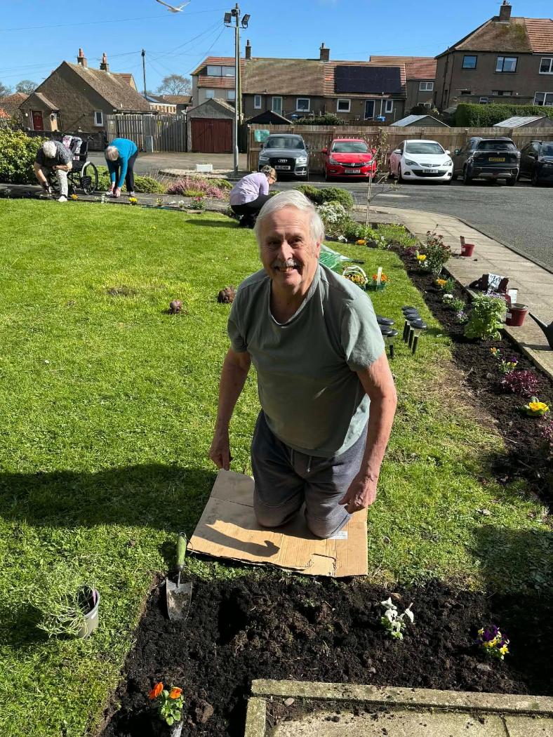 older man kneeling on ground gardening and smiling