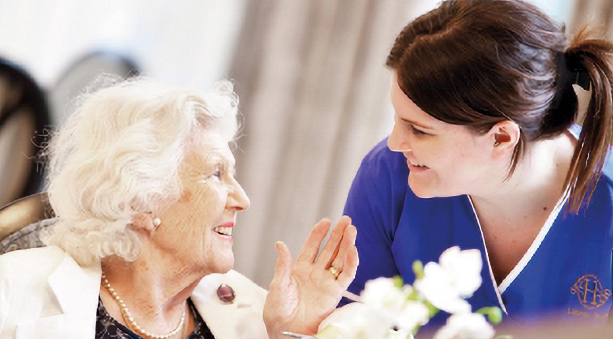 care home nurse in blue uniform smiles with an elderly woman
